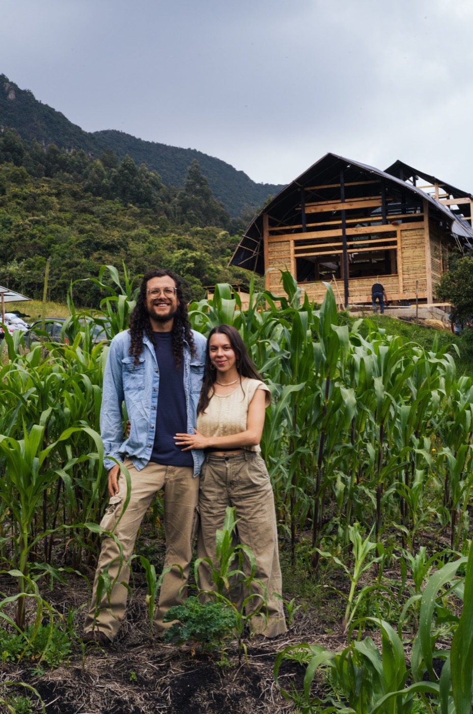 David y María entre el maíz de Finca Ocelote, con la cabaña de madera al fondo.